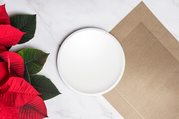 Christmas poinsettia with white plate placemat on gold placemat marble background