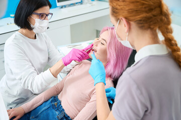 Orthodontist woman and assistant adjust bracket system to young patient