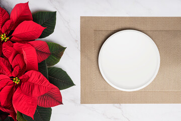 Christmas poinsettia with white plate placemat on gold placemat marble background