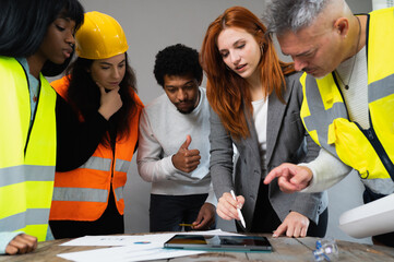 Group of five multiracial people working in a construction. Architects examining the project in the...