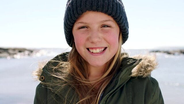 Child, smile and beach portrait in winter with coat for happy vacation, holiday travel or adventure outdoor in Dublin. Young girl, happiness and cold ocean journey for freedom break or seaside peace