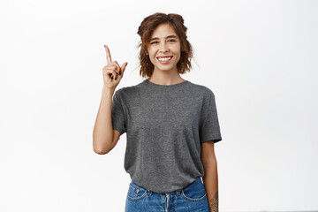 Happy smiling young woman pointing finger up, showing advertisement, top sale promo, standing over white background