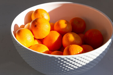 High angle selective focus still life of clementines in white ceramic bowl set on countertop in dappled light