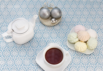 Traditional delicious brewed tea in a cup, teapot, snack marshmallows lie on table, a sweet dessert and Christmas decor