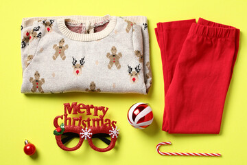 Naklejka premium Set of Christmas baby clothes on color background. Flat lay festive jumper, pants, merry Christmas eyeglasses and decorations. Kids New Year outfit.