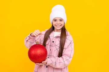 happy child in winter hat hold christmas decorative ball on yellow background, holiday