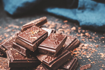 Dark chocolate bar pieces on dark background with grated chocolate, pile chunks of broken chocolate