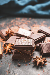 Dark chocolate bar pieces on dark background with grated chocolate and spices, pile chunks of broken chocolate