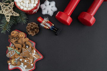 Gingerbread cookies, dumbbells, hot chocolate or cocoa with marshmallows, Christmas tree decorations. Fitness holiday season diet composition. Gym workout, dieting flat lay concept with copy space.