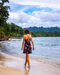 A beautiful girl in a dress walks on a paradise beach in Costa Rica on the Caribbean coast; relaxing on a tropical beach with palm trees by the Caribbean sea