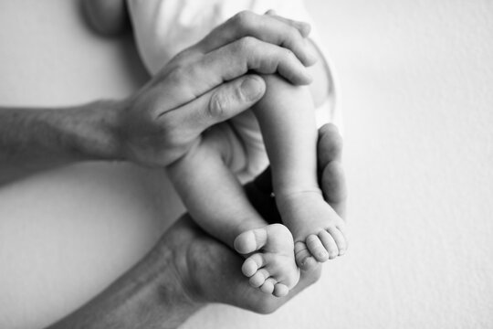 Baby feet in the hands of mother, father, older brother or sister, family. Feet of a tiny newborn close up. Little children's feet surrounded by the palms of the family. Black and white.