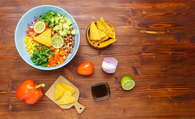 Fototapeta na wymiar Mexican vegetable salad, cowboy caviar in bowl with ingredients and nachos. Top view. Copy space