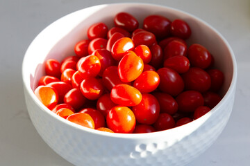 
High angle selective focus still life of cherry tomatoes in white ceramic bowl set on countertop in dappled light