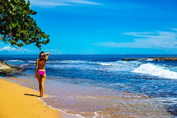 Obraz premium beautiful girl in a bikini walks on the sand on a Caribbean beach in Costa Rica; sunbathing on a paradise beach by the Caribbean sea, beach vacation in tropical Costa Rica