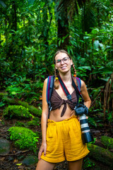 girl photographer walks through dense Costa Rican tropical rainforest; hiking through the jungle in...