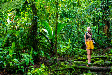 Naklejka na ściany i meble girl photographer walks through dense Costa Rican tropical rainforest; hiking through the jungle in Costa Rica's braulio carrillo national park near san jose