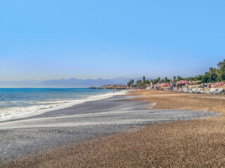 Antalya, Turkey - October 26,2019: People sunbathe on sun loungers under umbrellas at Lara Beach in Antalya. Wet footprint from the tide on the coarse clean sand on the shores of the Mediterranean Sea