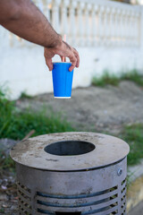 Male hand throwing a cardboard can into a metal dustbin outdoor