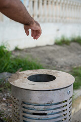 Male hand throwing a cardboard can into a metal dustbin outdoor