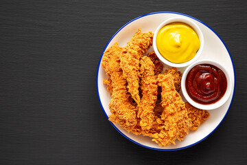 Homemade Chicken Strips with Mustard and BBQ on a Plate on a black background, top view. Flat lay, overhead, from above.