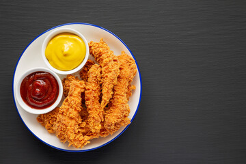 Homemade Chicken Strips with Mustard and BBQ on a Plate on a black background, top view. Flat lay, overhead, from above. Copy space.