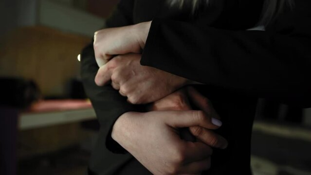 Cropped shot of a guy in hugs around the waist holding hands a girl in black sweater. Close-up hands together. Sensual shot.