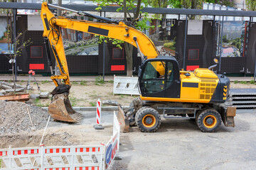 A large road wheeled excavator at a construction site in front of a fenced section of road.