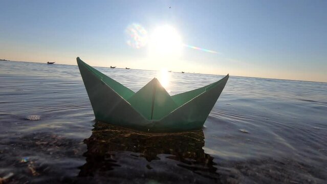 Man putting paper boat on surface of sea and it floating on waves at dawn close-up. A small paper boat sailing on sea on sunny summer day. Origami toy. Concept travel goal tourism dreaming travelling