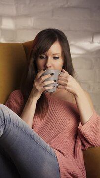 Casual woman relaxing at home sitting in armchair drinking coffee or tea.