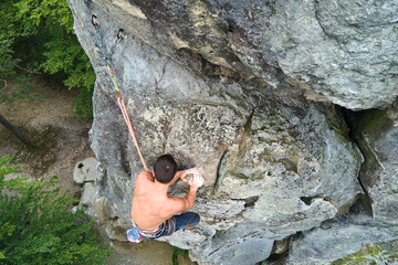 Determined climber clambering up steep wall of rocky mountain. Sportsman overcoming difficult...
