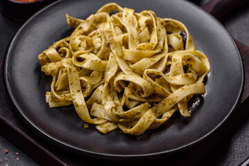 Delicious fresh pasta with pesto sauce and seafood on a black plate