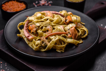 Delicious fresh pasta with pesto sauce and seafood on a black plate