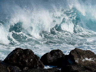 View of blue rolling wave slamming on volcanic rocks of the coastline like a tsunami. Beautiful...