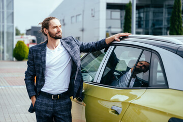 Young elegant fashionable man wearing plaid suit leaning on his car outdoor.