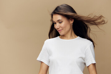 Obraz premium a beautiful cute attractive woman stands on a beige background with long hair developing in the wind, looking to the side with her head down.