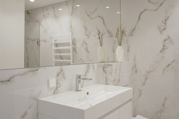 Modern minimalist white bathroom interior design with marble style tiles and white taps, vase and wall heater