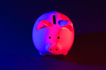 Piggy bank on a dark background with red-blue backlight. Banking concept. Bright neon lights on a black background