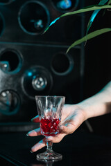 close-up of a girl's hand holding a glass by the stem. glass with a red drink on a black bar top.