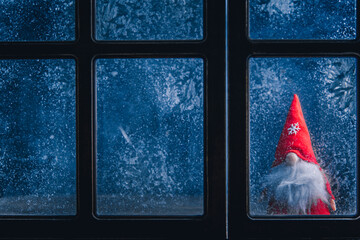 Christmas, winter composition. Christmas Gnome behind a frozen window