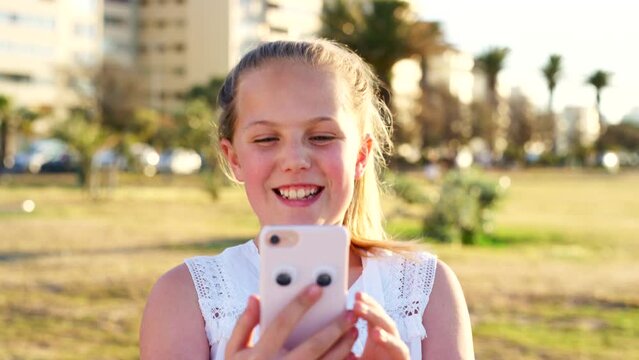 Child, phone and nature park while happy and laughing at funny video, game or internet post outdoor for fun and communication online. Girl kid with green background in California while on smartphone