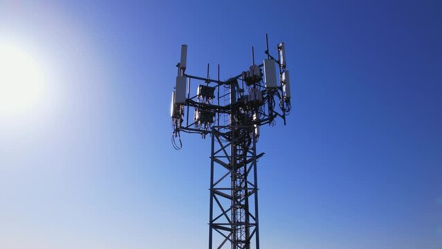 Aerial view of tower antennas with telecommunication, cell phone and radio transmitters. Around view at golden hour evening with sun leaks. Cellular signals for 5g, 4g mobile data and smart phones.