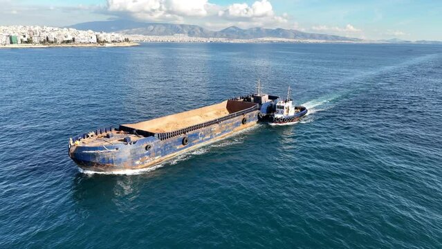 Aerial drone video of assisted with tug boat empty barge boat cruising in deep blue sea