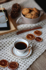 Cup of tea, books, tablet, bowl of cookies, various spices, pine cones and lit candles. Hygge at home. Selective focus.