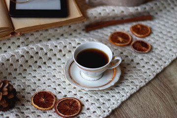 Cup of tea, books, tablet, bowl of cookies, various spices, pine cones and lit candles. Hygge at home. Selective focus.