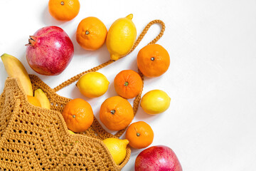 Fresh organic fruits in a yellow crochet bag on a white bacground. Eco friendly shopping and healthy eating concept. Copy space.
