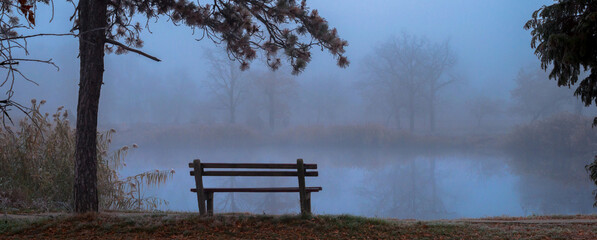 Creepy winter landscape showing bench beside lake on misty day
