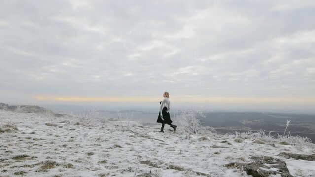 a woman walks alone on the edge of a cliff with an incredible winter view, admires nature and landscapes, the atmosphere of a Christmas fairy tale, a walk in nature on a frosty day