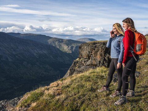 Two women using their cell phones and exploring the mountains and wilderness of the Yukon around Haines Junction; Yukon, Canada - Powered by Adobe