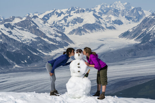 Women kissing the cheeks of a snowman on a mountaintop in Kluane National Park and Reserve; Haines Junction, Yukon, Canada