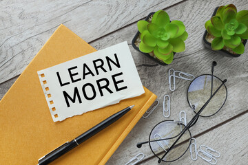 Learn More torn paper with text on a light wooden background. glasses potted plant